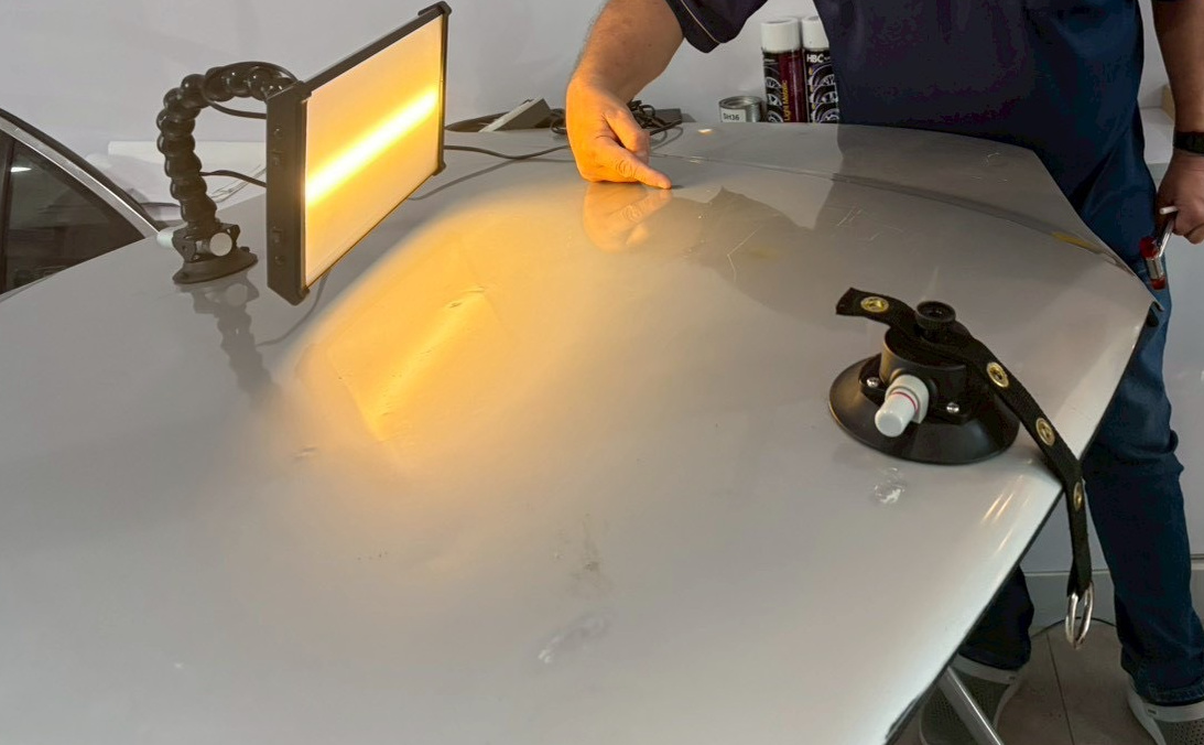 A close view of the grey panel shows a warm lamp reflection, surface marks and a suction fixture. A trainer's finger indicates part of the panel; this photograph does not classify the marks as highs or lows.