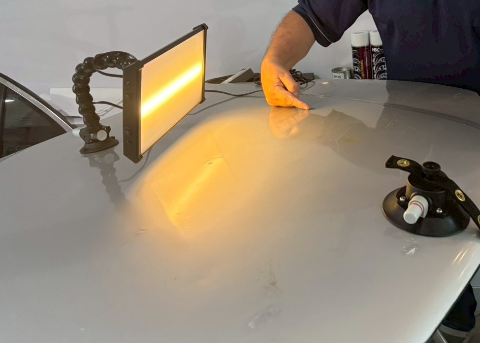 The upright yellow lamp is above the left edge of the grey panel. Its warm reflected band lies on the panel below it, separate from the lamp itself.