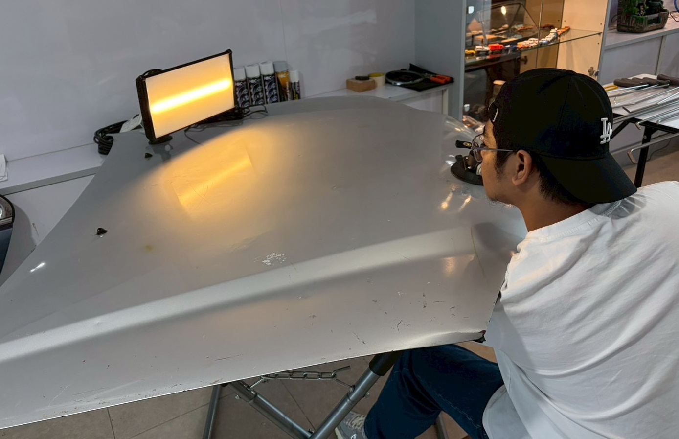 View A: a seated observer on the right looks across the panel towards a lamp. From this higher camera view, a broad warm reflected patch is visible on the left half of the panel.